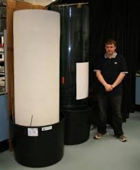 Photo of a researcher standing by two transparent tubes of water in which acrilic spheres can be dropped
